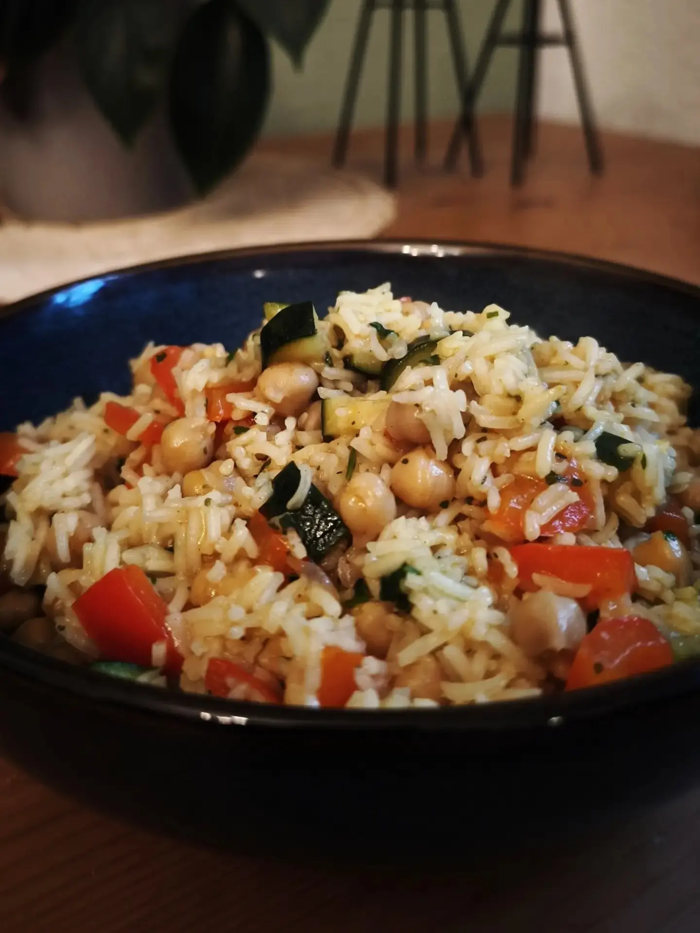 Nahaufnahme eines veganen One-Pot-Gerichts mit Basmatireis, Kichererbsen, Paprika und Zucchini in einer blauen Schale, garniert mit frischer Petersilie – gesundes, pflanzliches Mittagessen.